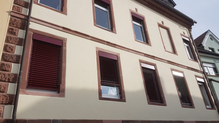 Das Bild zeigt einen Altbau nach abgeschlossener Altbausanierung. Hier wurden die Farben Creme für die Fassade und Rot für die Fensterrahmen gewählt.